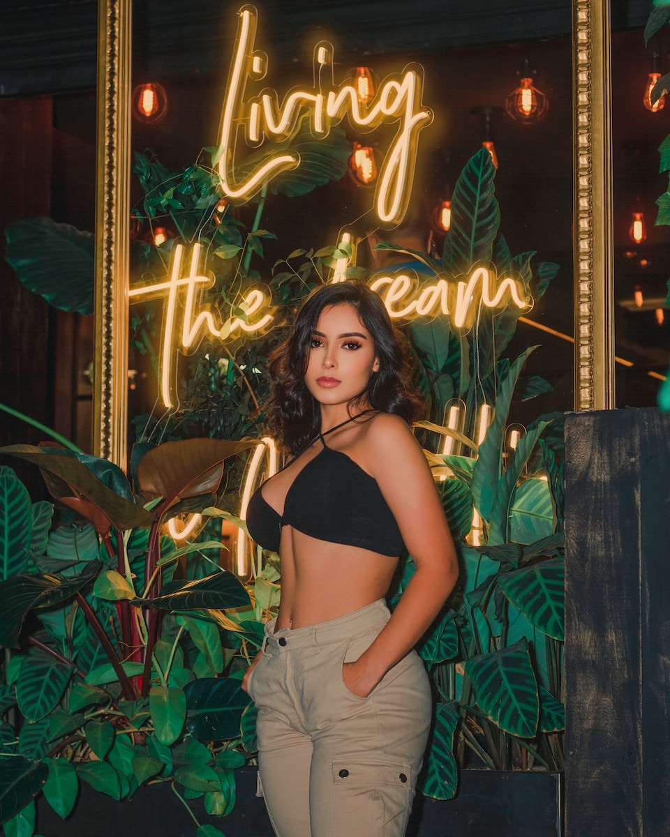 woman in black brassiere and white pants standing beside green plants