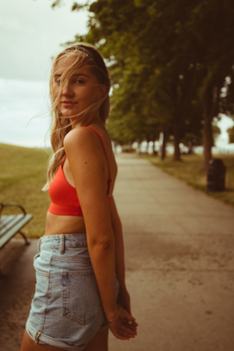 woman in red sports bra and blue denim shorts standing on gray concrete road during daytime