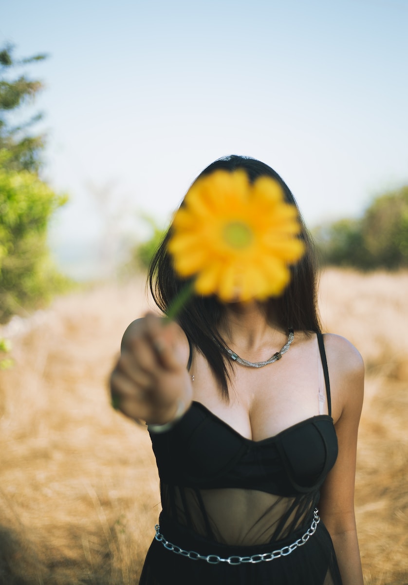 woman in black spaghetti strap top holding yellow sunflower during daytime